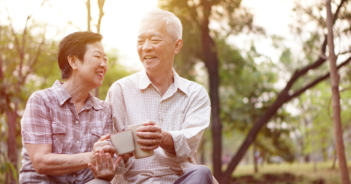 Elderly couple enjoying their senior citizen discounts, smiling and having a drink while sitting at the park.