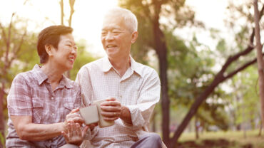 Elderly couple enjoying their senior citizen discounts, smiling and having a drink while sitting at the park.