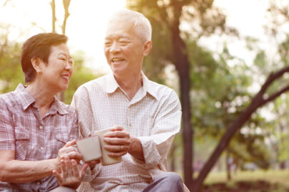 Elderly couple enjoying their senior citizen discounts, smiling and having a drink while sitting at the park.